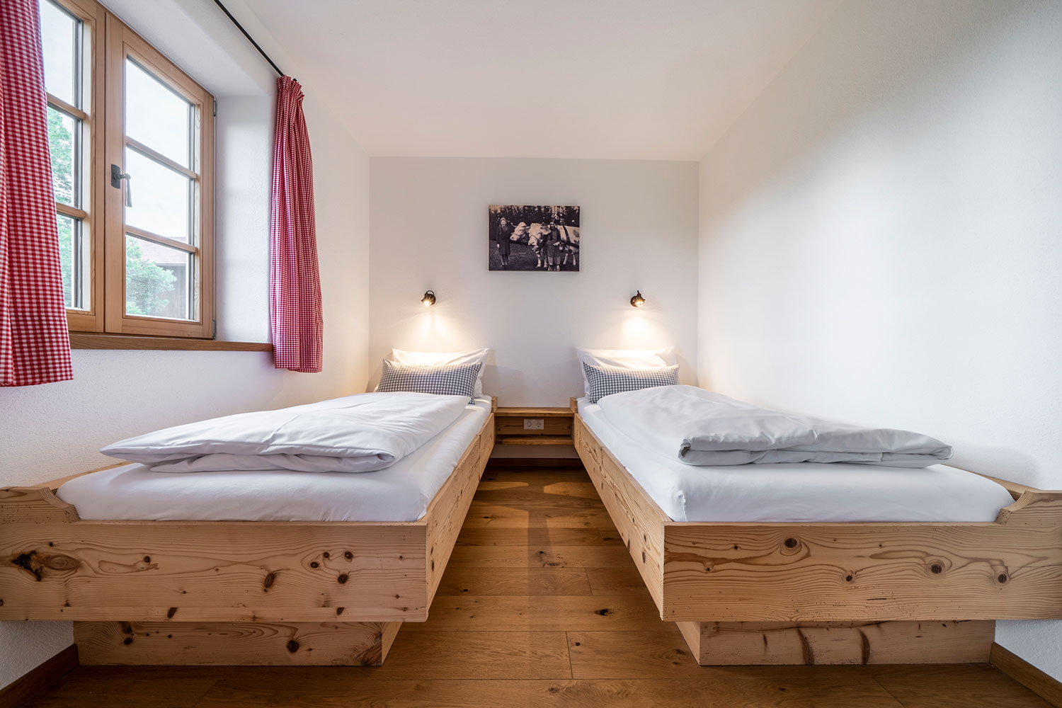 Schlafzimmer mit zwei getrennten Betten aus Holz und Fenster mit roten vorhängen