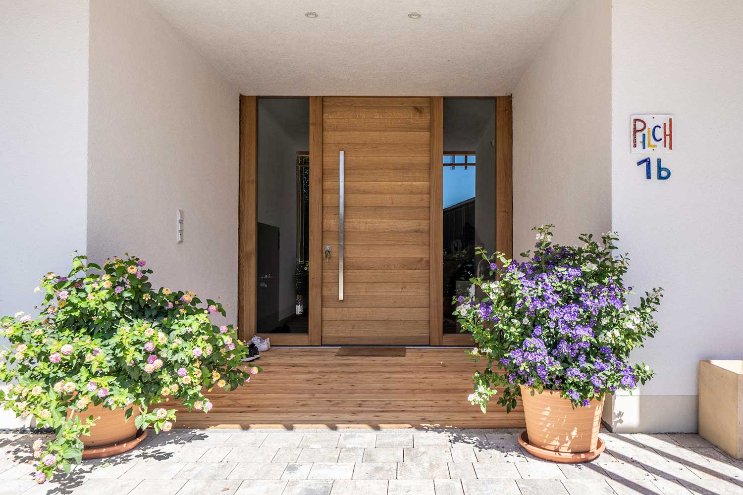 Eingangsbereich mit Holztüre und Blumenstöcke